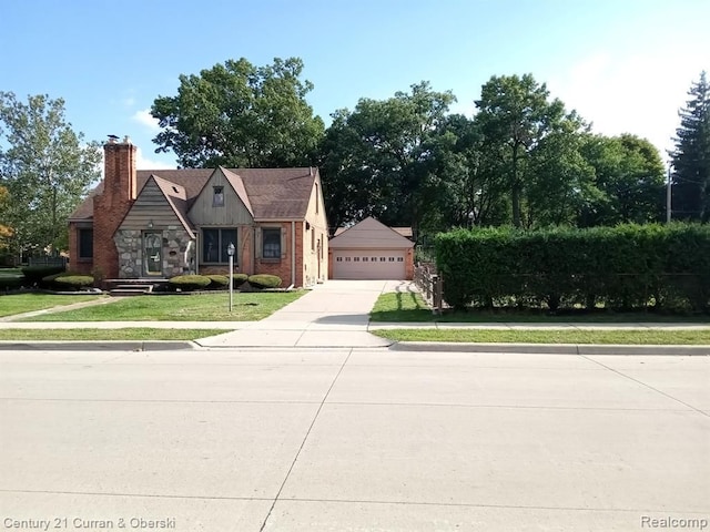 view of front of house with brick siding, a detached garage, stone siding, a front lawn, and a chimney