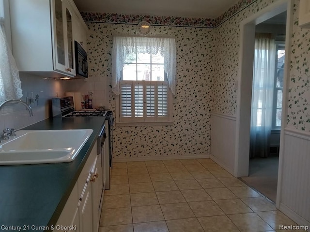 kitchen with dark countertops, glass insert cabinets, stove, white cabinetry, and a sink