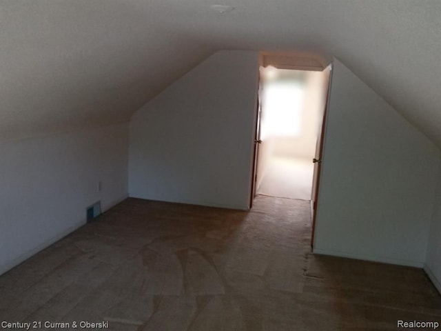 additional living space featuring lofted ceiling, dark carpet, and visible vents