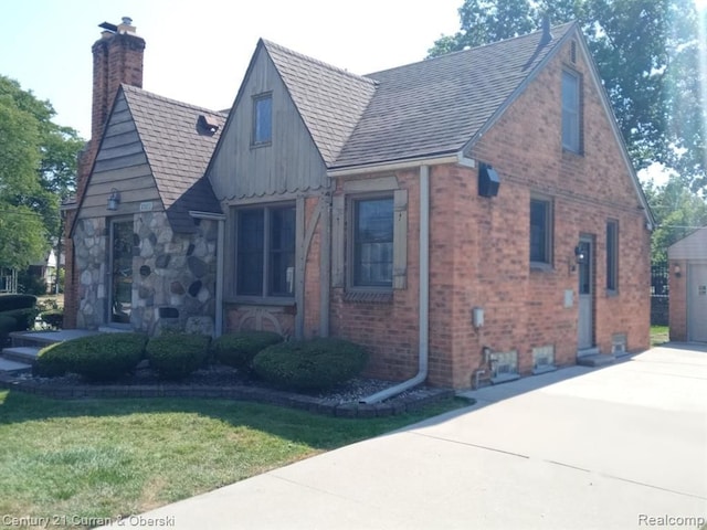 view of front facade featuring a garage, brick siding, a shingled roof, a chimney, and a front yard