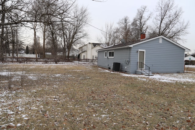 snow covered property with entry steps, central AC unit, and a chimney