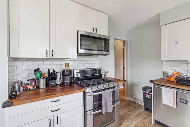 kitchen featuring stainless steel appliances, butcher block countertops, baseboards, white cabinets, and light wood-type flooring