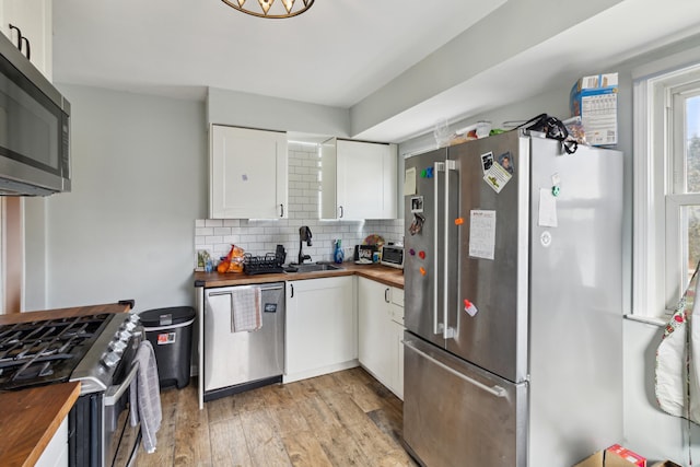 kitchen featuring stainless steel appliances, tasteful backsplash, wooden counters, white cabinetry, and a sink