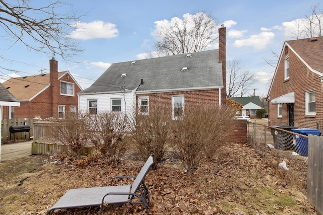 rear view of property featuring brick siding, fence, and roof with shingles