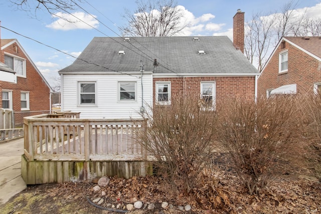 rear view of house featuring roof with shingles, brick siding, a chimney, and a wooden deck