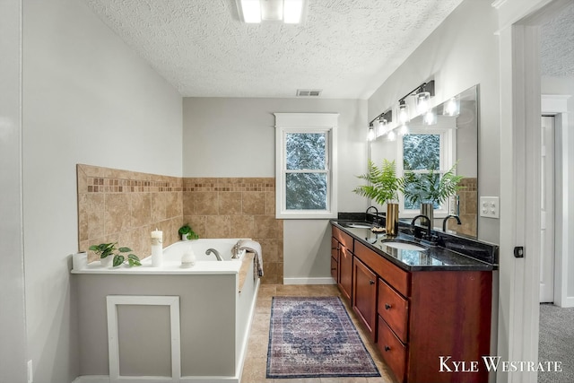 full bath featuring a textured ceiling, a sink, visible vents, a bath, and double vanity