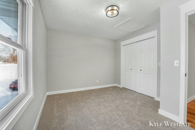 unfurnished bedroom featuring attic access, baseboards, a textured ceiling, carpet flooring, and a closet