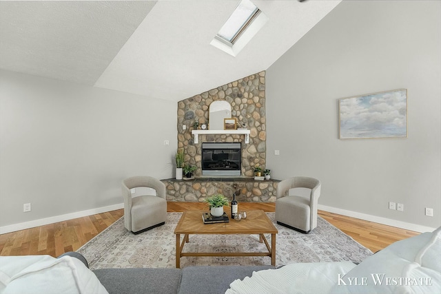 living area featuring lofted ceiling with skylight, a stone fireplace, baseboards, and wood finished floors