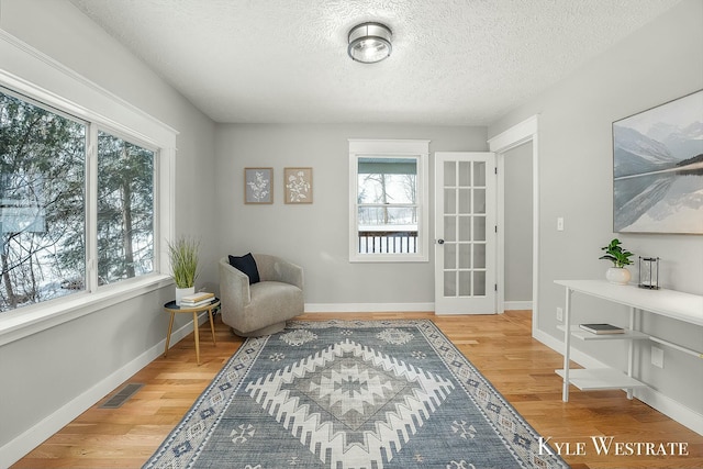 living area with baseboards, a textured ceiling, visible vents, and wood finished floors