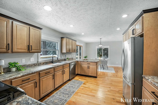 kitchen with light wood-style flooring, stainless steel appliances, a sink, hanging light fixtures, and brown cabinetry