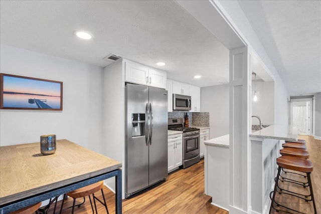 kitchen with stainless steel appliances, visible vents, white cabinetry, backsplash, and light wood finished floors