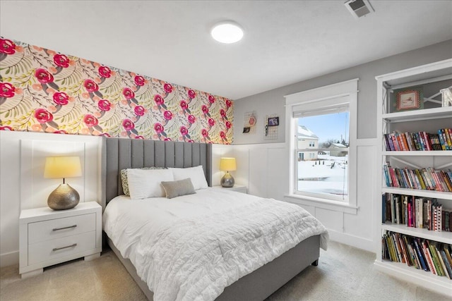 bedroom with wainscoting, visible vents, a decorative wall, and light carpet