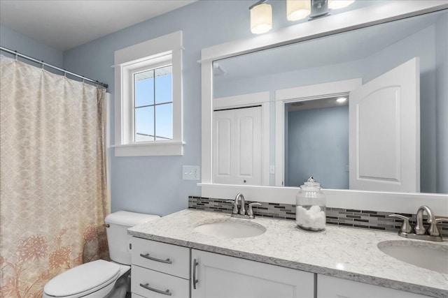 bathroom featuring double vanity, toilet, decorative backsplash, and a sink