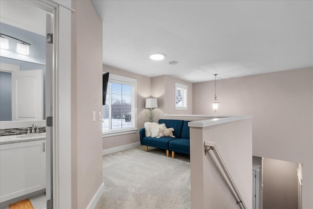 sitting room with baseboards, light colored carpet, and an upstairs landing