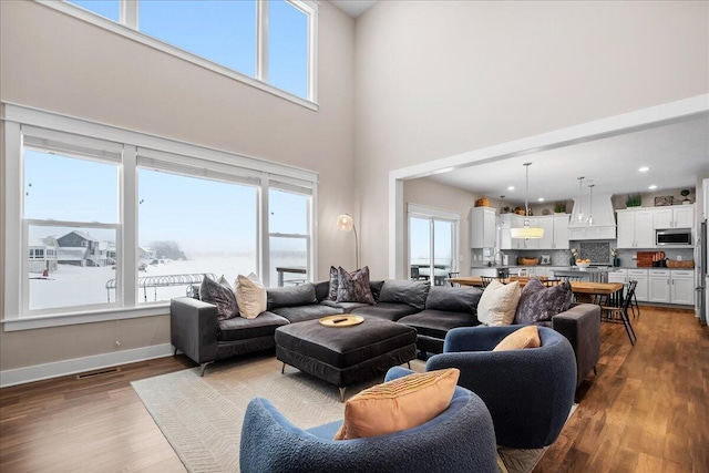 living area featuring a towering ceiling, wood finished floors, visible vents, and baseboards