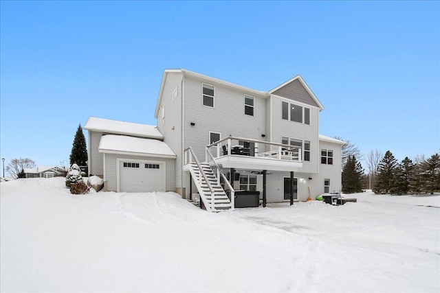 snow covered rear of property with a garage, stairway, and a wooden deck