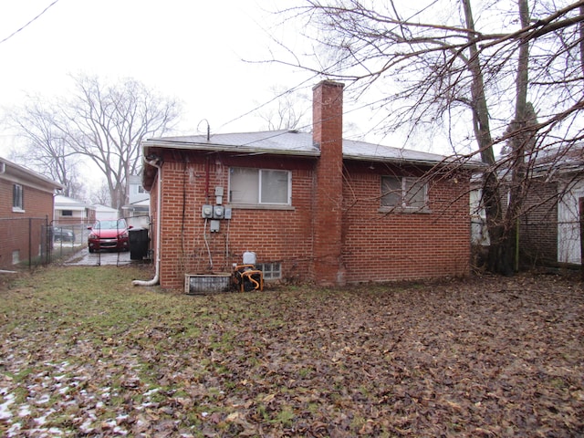 back of house with a chimney, fence, and brick siding