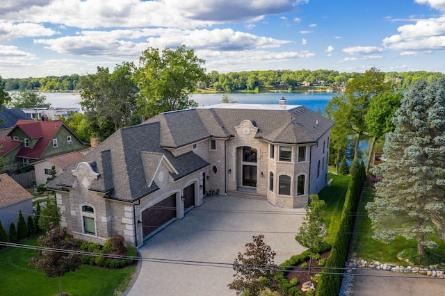 view of front facade with concrete driveway, stone siding, a chimney, and a water view