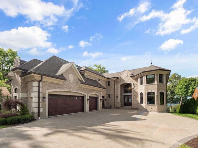 french country home with a garage, brick siding, driveway, french doors, and roof with shingles