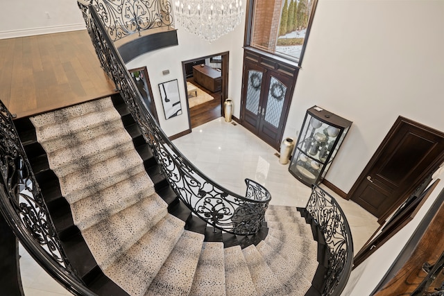 stairway with a chandelier, french doors, a towering ceiling, and baseboards