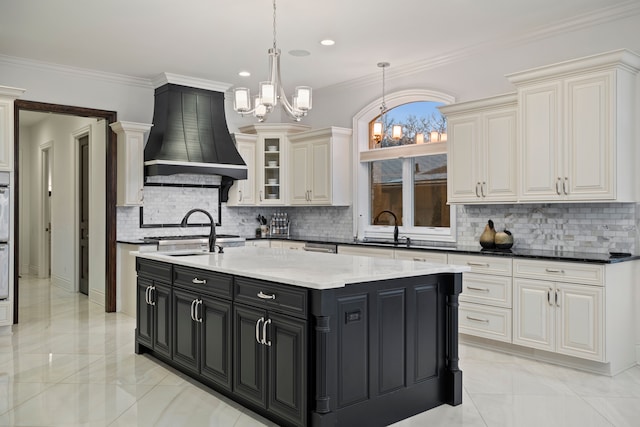 kitchen featuring a kitchen island with sink, dark cabinets, a sink, custom range hood, and crown molding