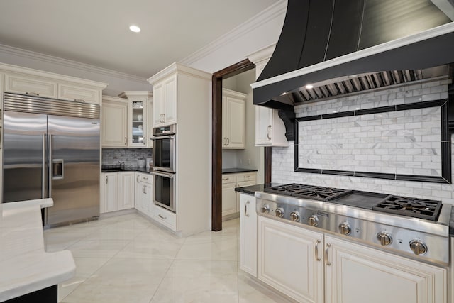 kitchen featuring tasteful backsplash, wall chimney exhaust hood, glass insert cabinets, appliances with stainless steel finishes, and crown molding