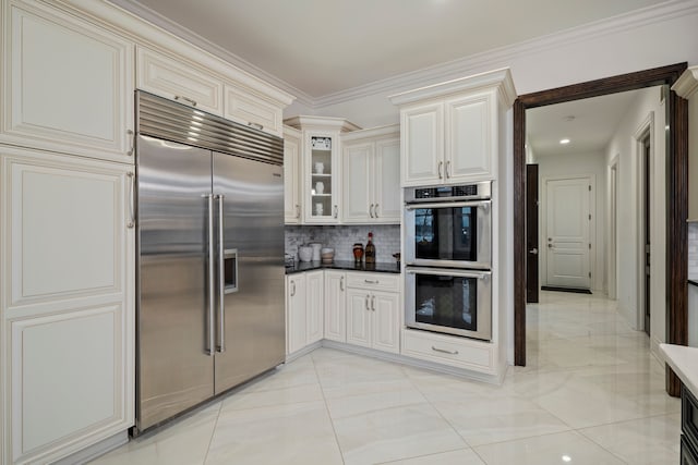 kitchen with dark countertops, glass insert cabinets, ornamental molding, stainless steel appliances, and backsplash