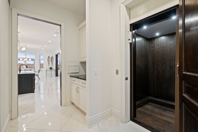 corridor featuring light tile patterned floors, elevator, a sink, a chandelier, and baseboards