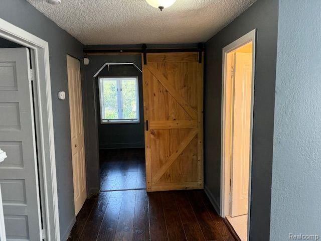 hall with dark wood-style floors, a textured ceiling, baseboards, and a barn door