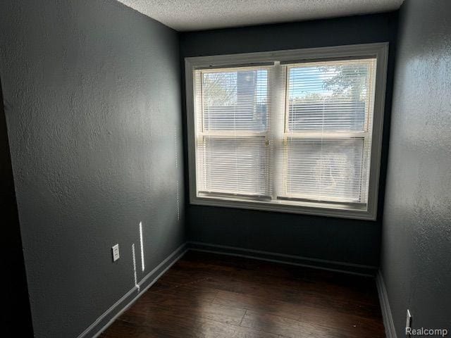 empty room featuring dark wood-style floors, a textured wall, a textured ceiling, and baseboards