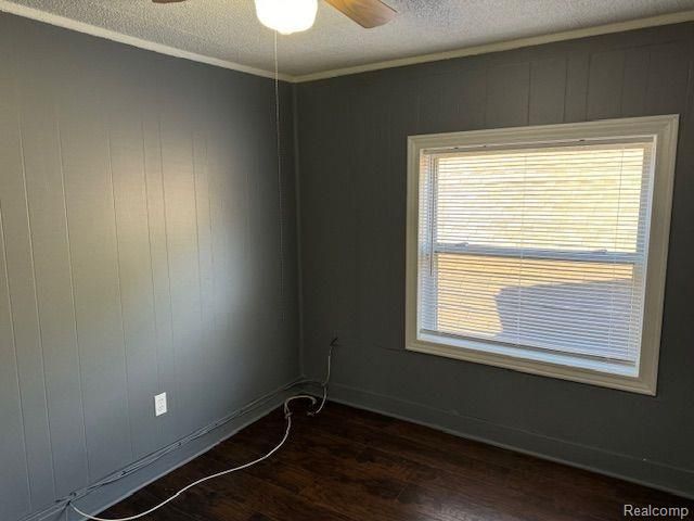 unfurnished room with a ceiling fan, crown molding, dark wood finished floors, and a textured ceiling