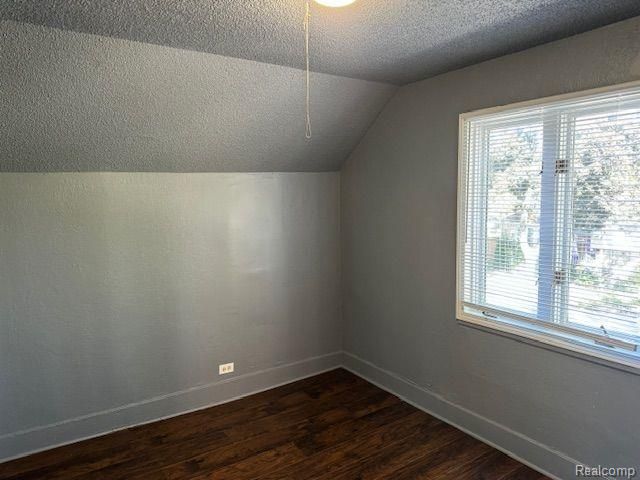 additional living space featuring a textured ceiling, baseboards, vaulted ceiling, and dark wood-type flooring