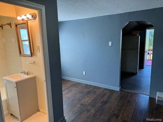 interior space with arched walkways, a textured wall, a textured ceiling, wood finished floors, and a sink