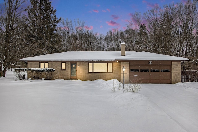 ranch-style home with an attached garage, a chimney, and brick siding