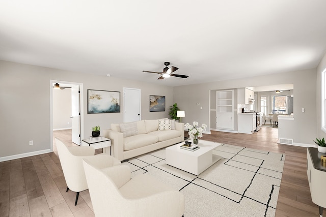 living room with light wood-type flooring, baseboards, visible vents, and ceiling fan