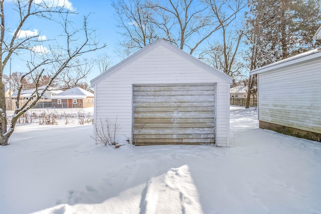 snow covered garage featuring a garage and fence