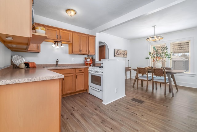 kitchen with arched walkways, white range with gas stovetop, a sink, light wood finished floors, and pendant lighting