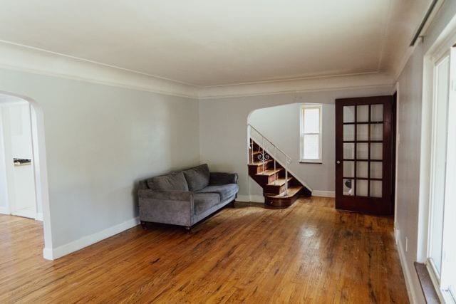 unfurnished room featuring baseboards, arched walkways, wood finished floors, stairs, and crown molding