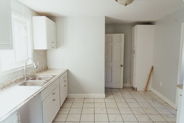 kitchen with backsplash, white cabinetry, light countertops, and a sink