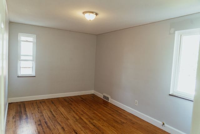 spare room with dark wood-type flooring, visible vents, and baseboards