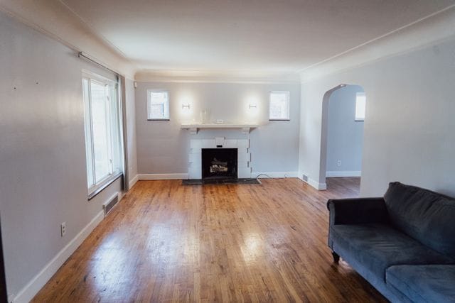 unfurnished living room featuring arched walkways, wood finished floors, a fireplace with flush hearth, visible vents, and baseboards