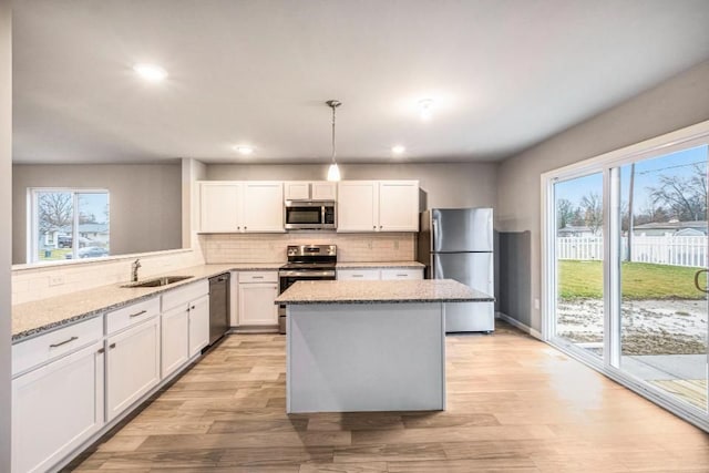 kitchen featuring white cabinets, light wood-style flooring, a kitchen island, stainless steel appliances, and a sink