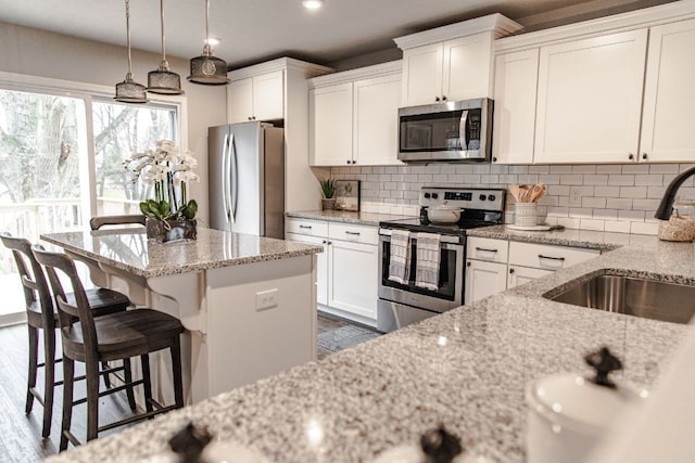 kitchen featuring stainless steel appliances, tasteful backsplash, white cabinetry, a sink, and light stone countertops