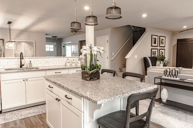 kitchen with a breakfast bar, pendant lighting, light wood finished floors, white cabinetry, and a sink