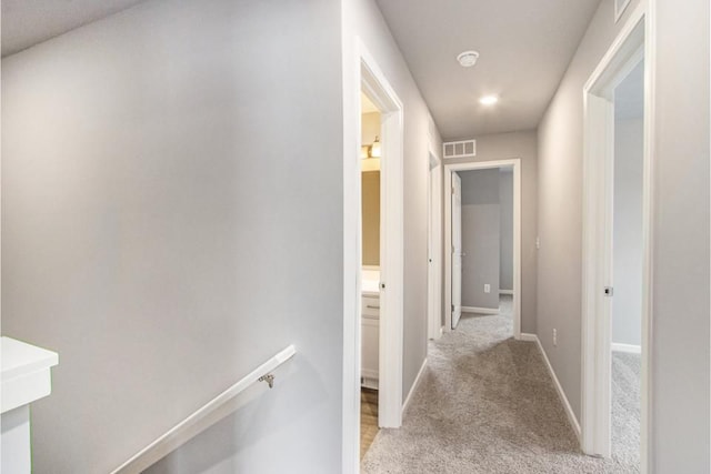 hallway featuring an upstairs landing, light colored carpet, visible vents, and baseboards