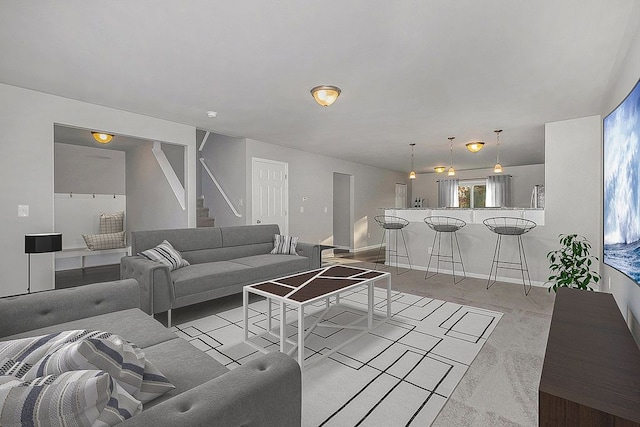 living room featuring light carpet, baseboards, and stairs