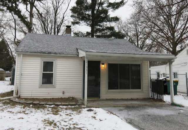 snow covered back of property featuring a chimney, fence, and roof with shingles