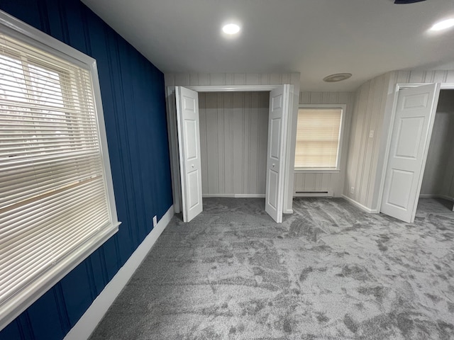 unfurnished bedroom featuring a baseboard heating unit, a closet, light carpet, and baseboards