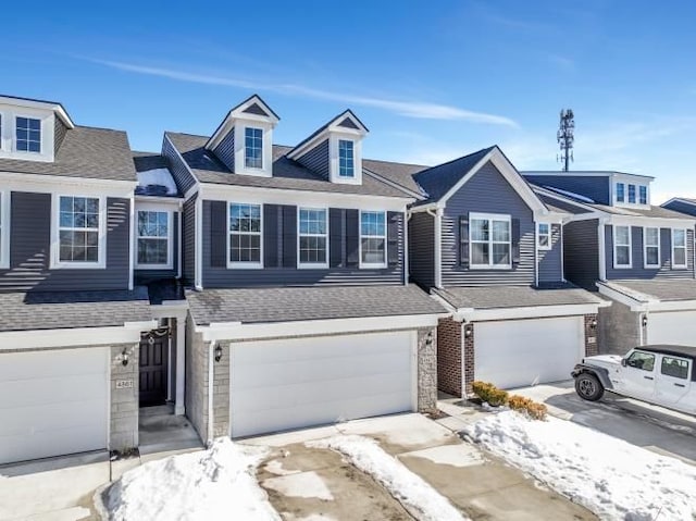 townhome / multi-family property featuring an attached garage, stone siding, and roof with shingles