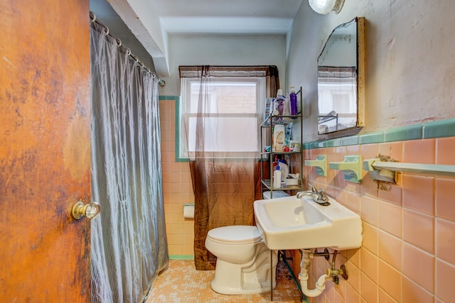 bathroom with tile walls, toilet, a sink, a shower with curtain, and tile patterned floors